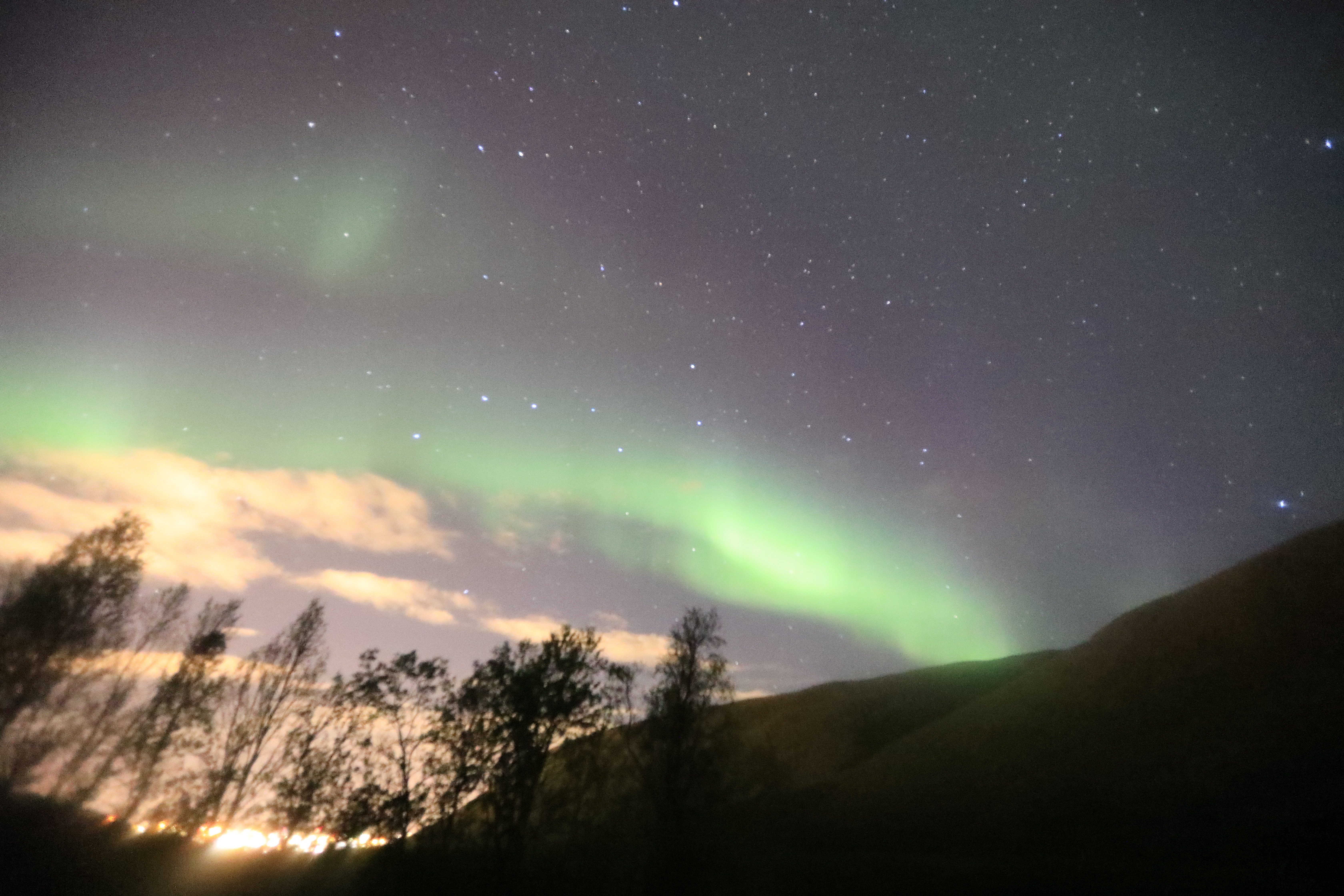 オーロラと星々、木々、雲、街の明かり１（16mm、F2.8、ISO32000、2.5秒）
